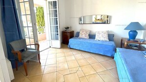 A room with a sofa, a chair, a small table with a lamp, and a sliding glass door leading to an outdoor area.