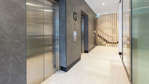 A modern hallway with elevators, a staircase, and a glass wall. - Haberfield Hotel (Haberfield)