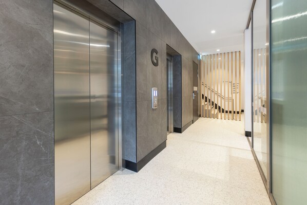 A modern hallway with elevators, a staircase, and a glass wall. - Haberfield Hotel (Haberfield)