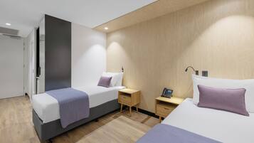 A modern hotel room with two beds, wooden flooring, and a built-in wardrobe.
