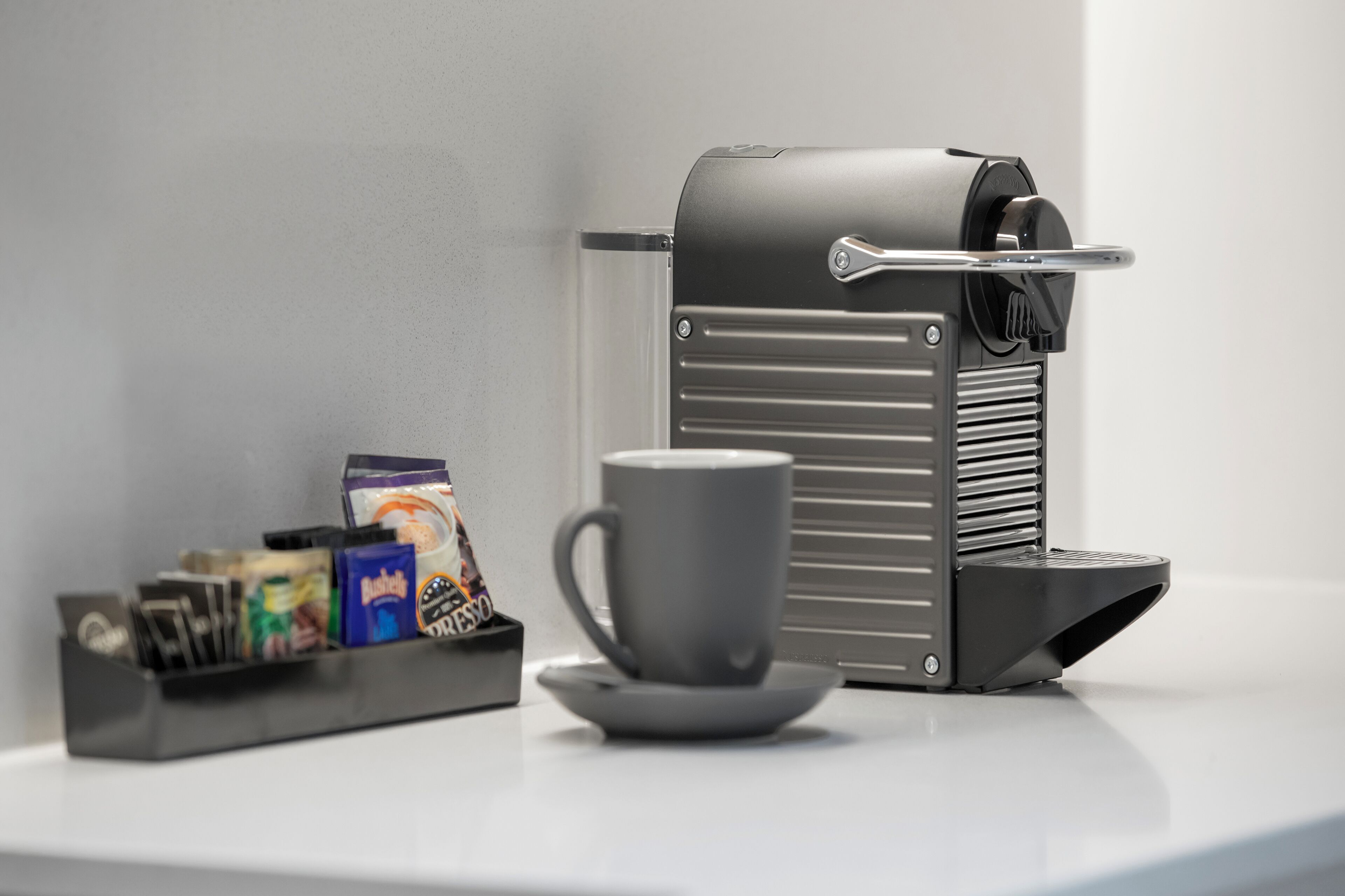 Une machine à café avec une tasse et un plateau de dosettes de café, le tout posé sur une surface blanche.