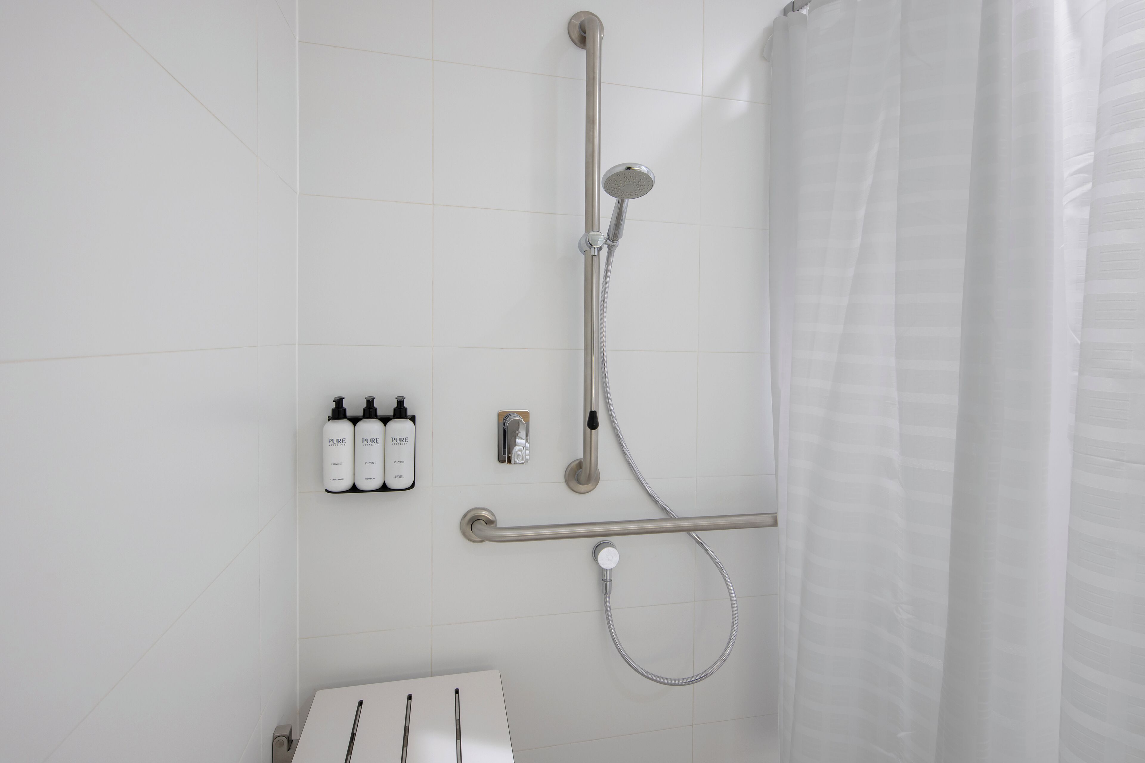 Un baño moderno con cabina de ducha, barra de apoyo y toallero con botellas.