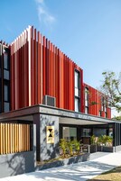 Un hotel moderno con una fachada roja llamativa, un logo visible y un área exterior bien cuidada con plantas.