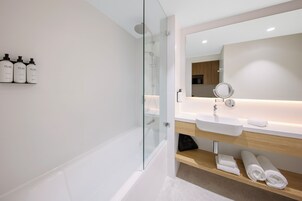 Un baño moderno con ducha de vidrio, un lavabo blanco y un espejo encima. Hay tres botellas de champú Pure en la pared.