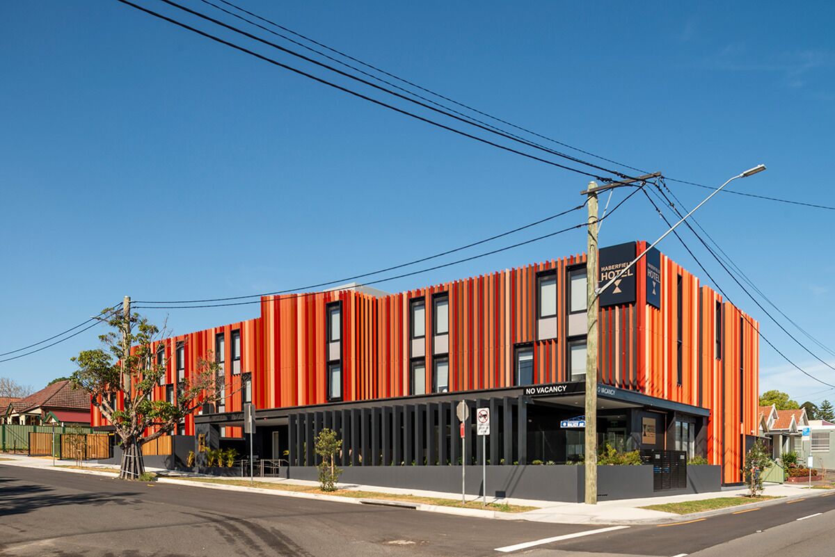 A modern building with a red facade and black windows, labeled "HABERFELD HOZL HOTEL."