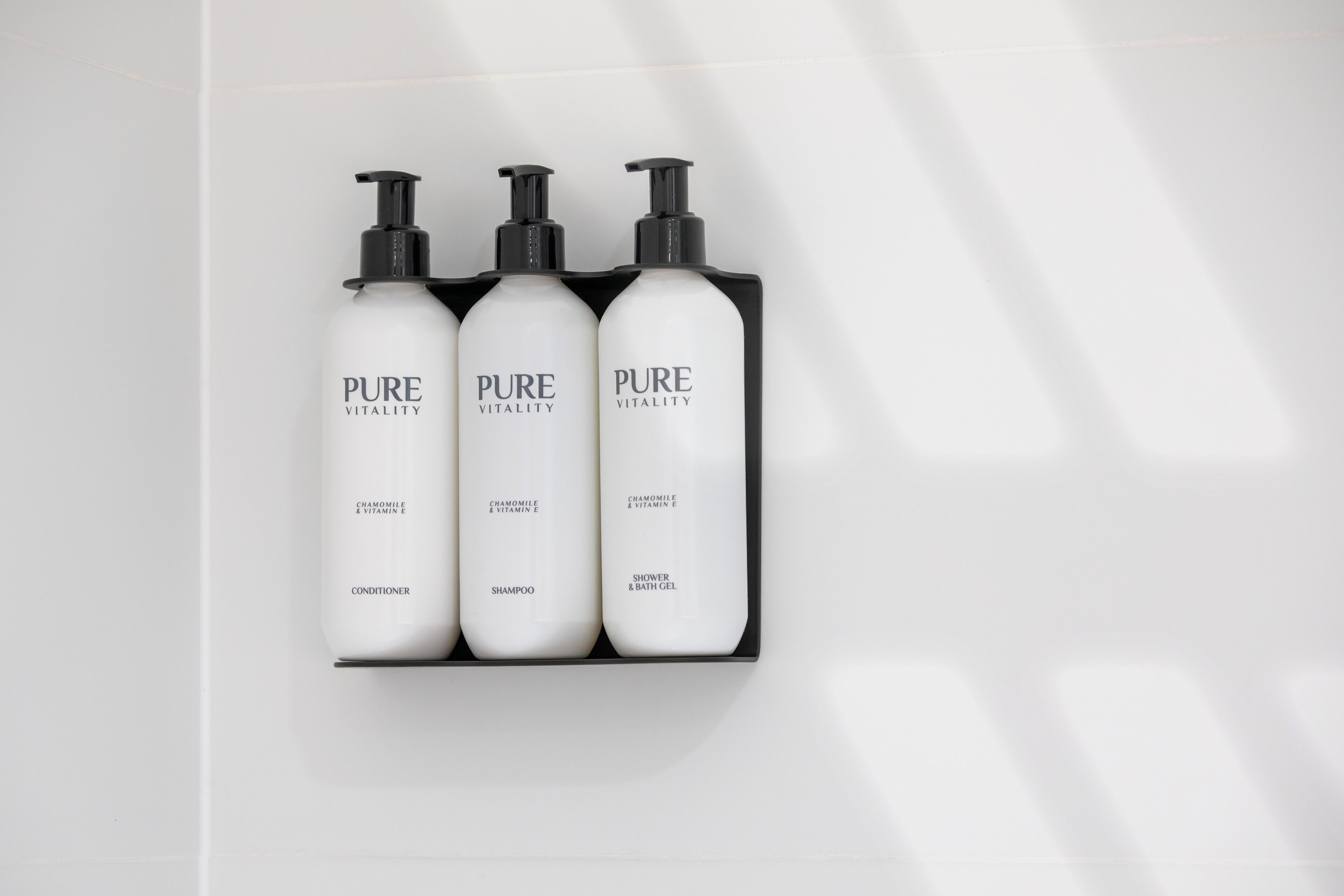 Three bottles of PURE VITALITY products: conditioner, shampoo, and shower & bath gel, arranged on a white surface.