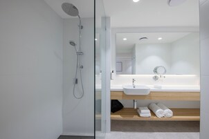 Un bagno moderno con cabina doccia in vetro, lavabo bianco e ripiano in legno con asciugamani.
