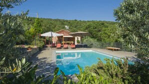 A poolside area with a pool, lounge chairs, and a small building with a roof.