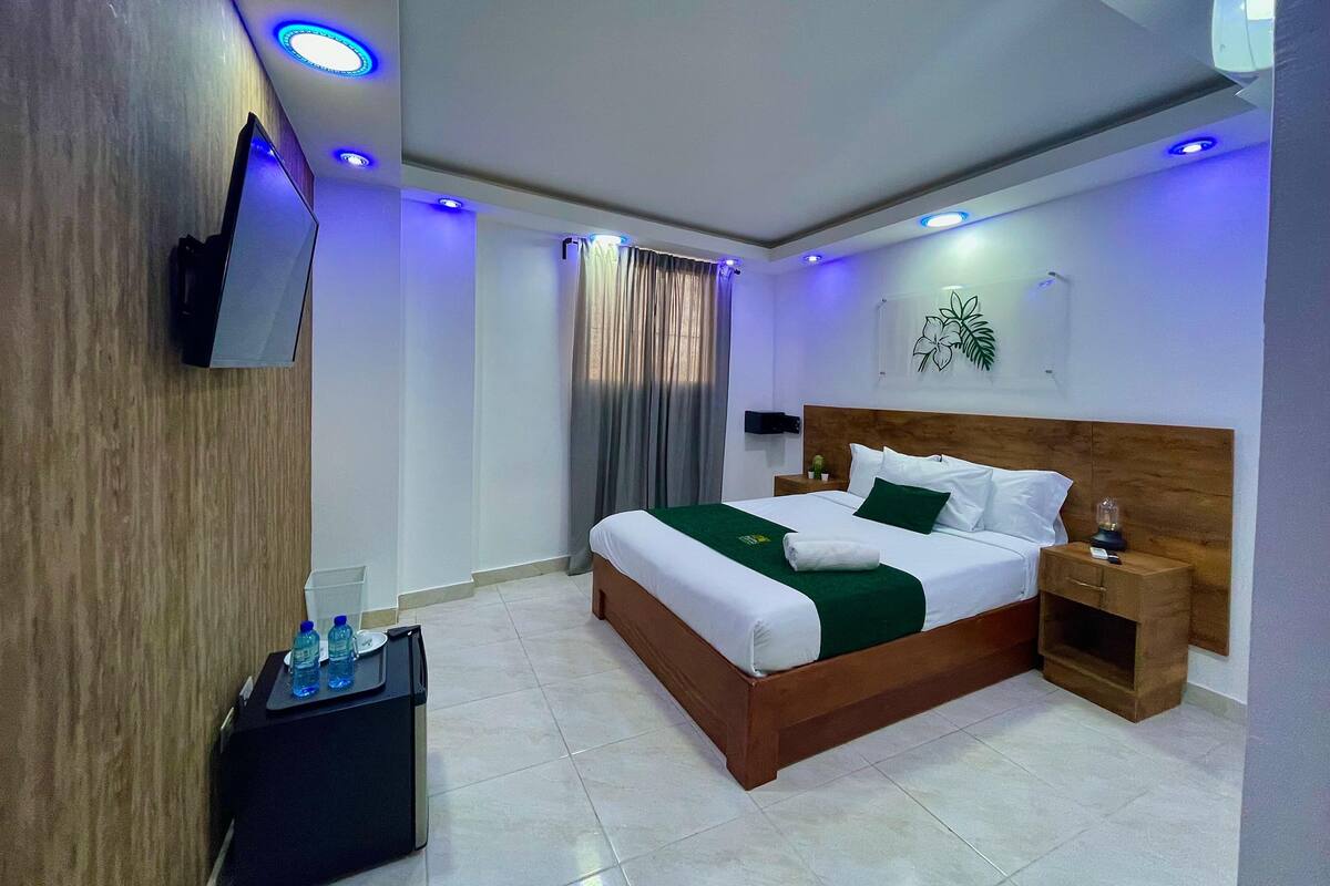 A hotel room with a bed, bedside tables, a TV, and a water dispenser.