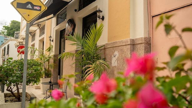 A building with a yellow and beige facade, a black awning, and a sign indicating a steep road ahead. - Jardin Colonial Boutique Hotel (Santo Domingo)