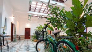 A spacious indoor area with a tiled floor, a bicycle, and various plants. - Jardin Colonial Boutique Hotel (Santo Domingo)