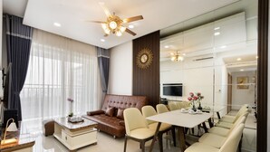 A modern living room with a brown leather sofa, beige chairs, a glass coffee table, and a dining table with chairs. - Golden Mansion Apartments Phu Nhuan (Ho Chi Minh City)