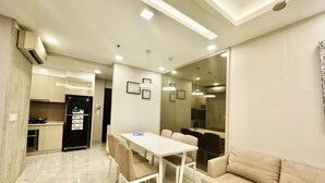 A modern kitchen with a refrigerator, stove, and microwave. There is a dining area with a table and chairs, and a sofa. The room has a tiled floor and a ceiling with recessed lighting. - Golden Mansion Apartments Phu Nhuan (Ho Chi Minh City)
