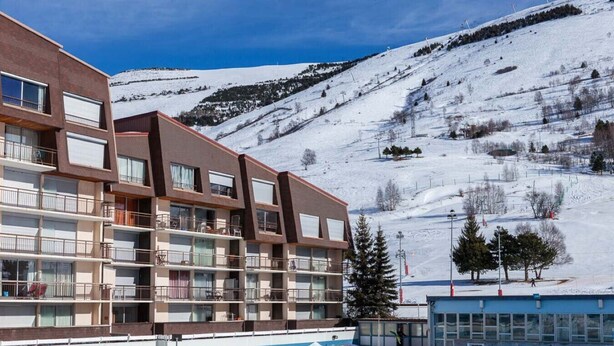 A multi-story hotel with balconies, a ski slope in the background, and a clear blue sky. - Studio 4 ppl, balcony, near the ski station (Les Deux Alpes)