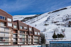 A multi-story hotel with balconies, a ski slope in the background, and a clear blue sky.