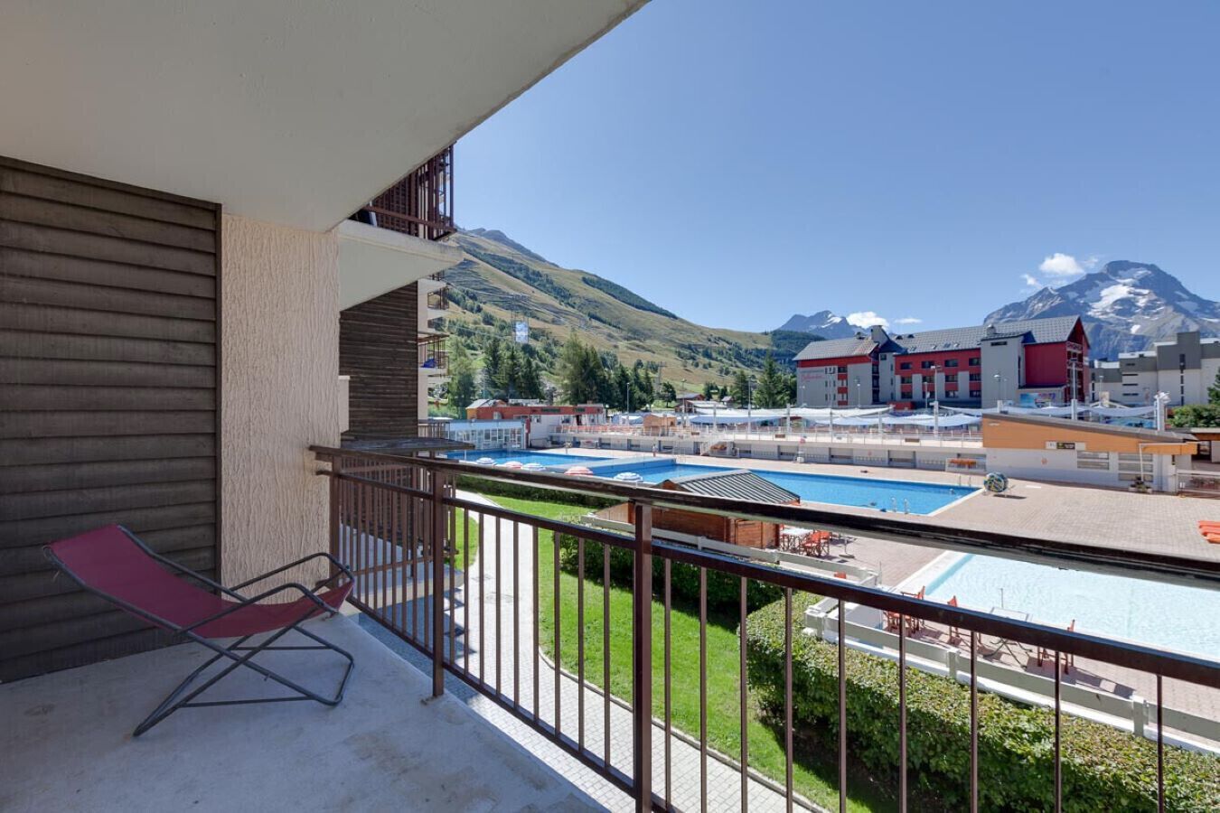 A balcony with a red chair, a pool area, and a mountain view.
