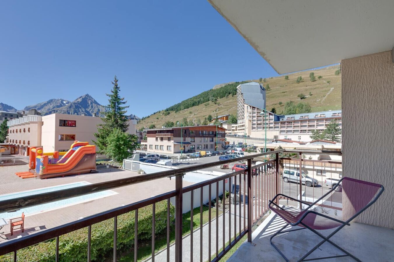Un balcone con vista su un parco giochi, edifici e montagne.