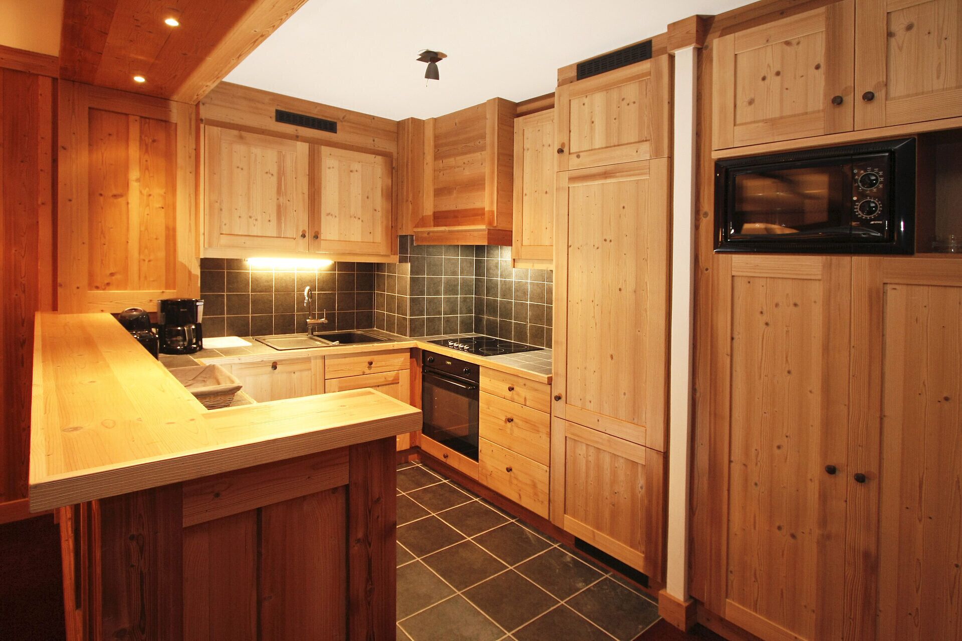 A kitchen with wooden cabinets, a black tiled backsplash, a built-in oven, and a microwave.