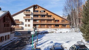 Ein mehrstöckiges Gebäude mit Balkonen, einem mit Schnee bedeckten Parkplatz und einem klaren Himmel.