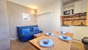 Ein gemütlicher Wohnbereich mit Sofa, Esstisch für zwei Personen, einer Küchenzeile mit Mikrowelle und einem kleinen Kühlschrank.