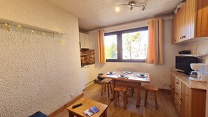 Eine kleine Küche mit Holzausstattung, einem Esstisch für vier Personen und einem Fernseher auf einem Holzschrank.