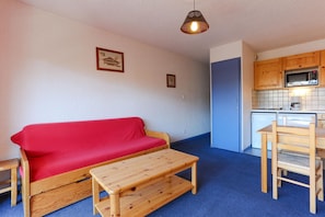 Um espaço de estar compacto com sofá vermelho, mesa de madeira, cozinha compacta e porta azul.