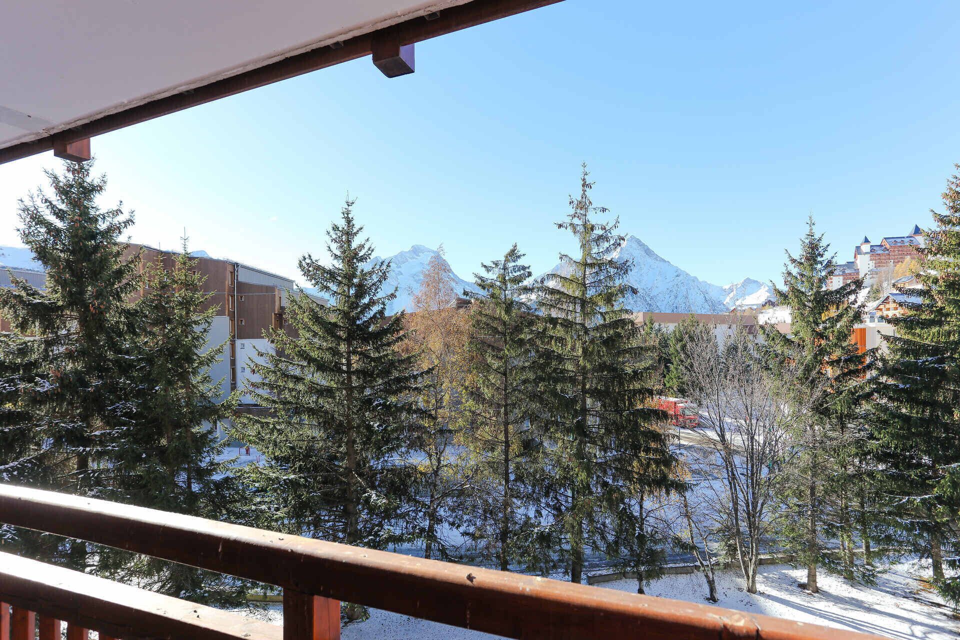 Vue sur des arbres et des montagnes enneigés, prise depuis un balcon.