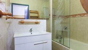 A bathroom with a white sink, a mirror, a shower with a glass door, and a wooden shelf above the sink. - Studio 4 ppl, splendid view from balcony (Les Deux Alpes)