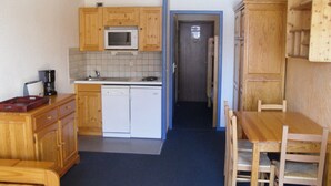 A compact kitchen with wooden cabinets, a microwave, a coffee maker, and a dishwasher. There is a dining area with a wooden table and chairs. - Studio 4 ppl, splendid view from balcony (Les Deux Alpes)