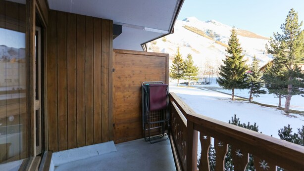 Un balcon en bois avec une chaise en métal et une porte en bois.