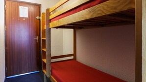 Un lit superposé avec un matelas rouge, une porte en bois avec une pancarte et un sol recouvert de moquette.