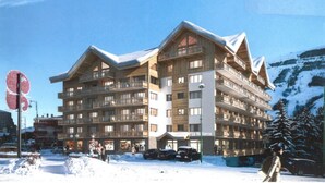 Een meerhoog hotel met balkons, een skigebied op de achtergrond en een besneeerd landschap.