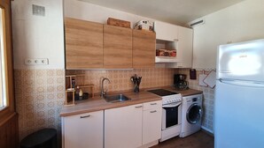 A compact kitchen with white cabinets, a sink, a stove, a washing machine, and a refrigerator.