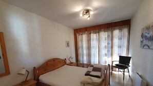 A bedroom with a wooden bed, bedside table, chair, and curtains.