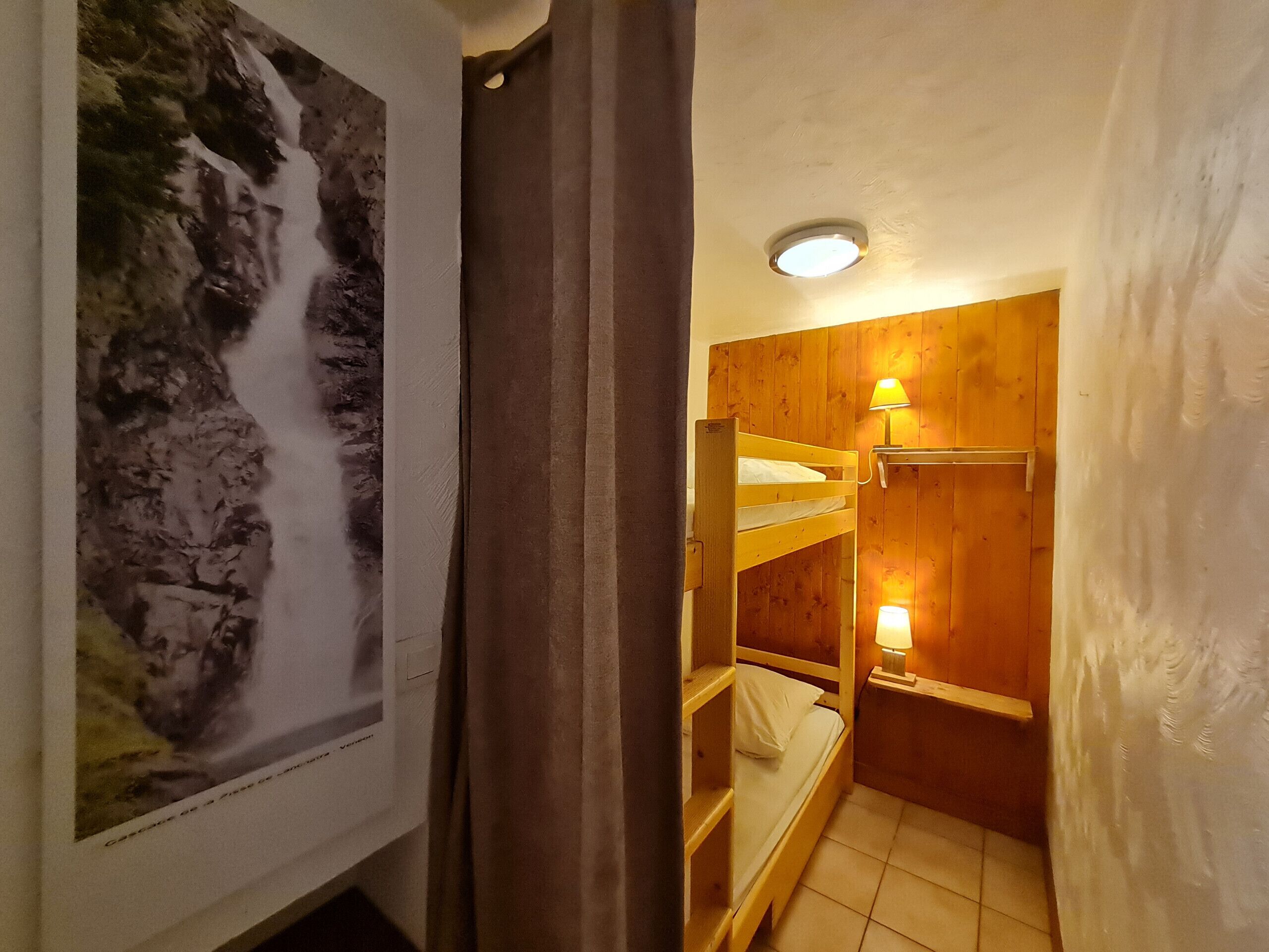 Una habitación pequeña y acogedora con literas, un cuadro enmarcado de una cascada y una lámpara en el techo.