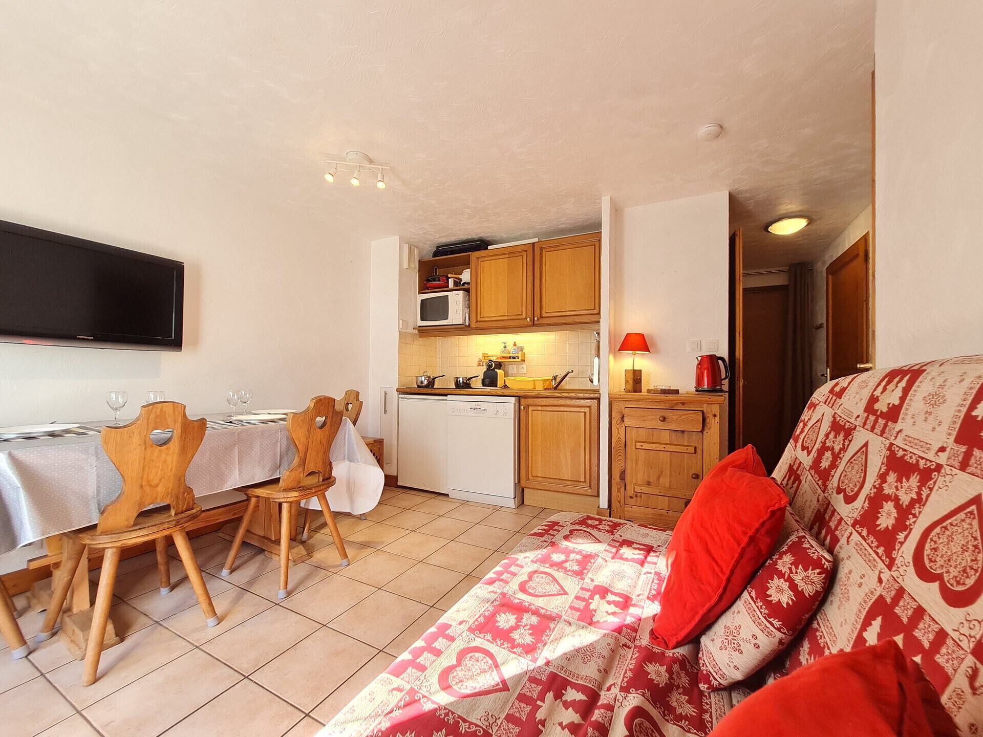 A compact living space with a dining area, kitchenette, and a sofa with patterned bedding.