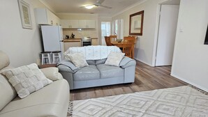 Una sala de estar con sofá, una mesa de comedor con sillas, una zona de cocina y un televisor montado en la pared.