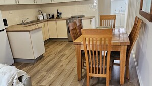 Una cocina compacta con armarios blancos, una mesa de comedor de madera y un refrigerador pequeño.