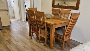 Un comedor con una mesa y sillas de madera, un espejo grande en la pared, y una cocina al fondo.