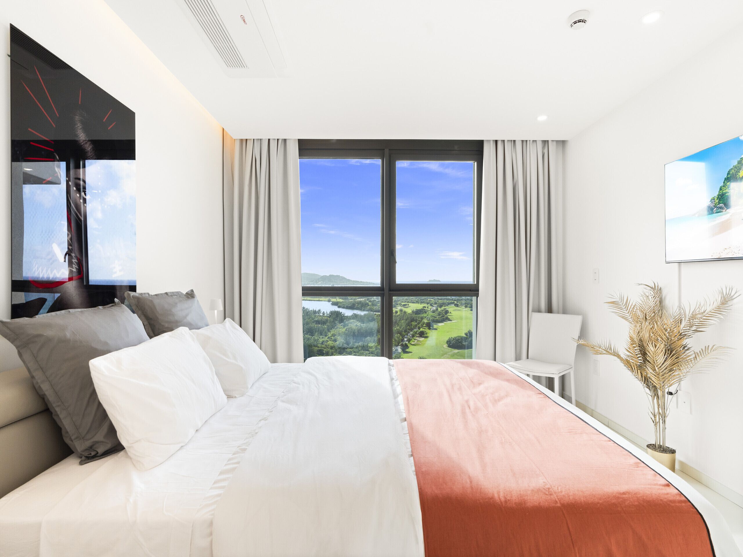 A hotel room with a large bed, a television, a view of a landscape, and a plant.