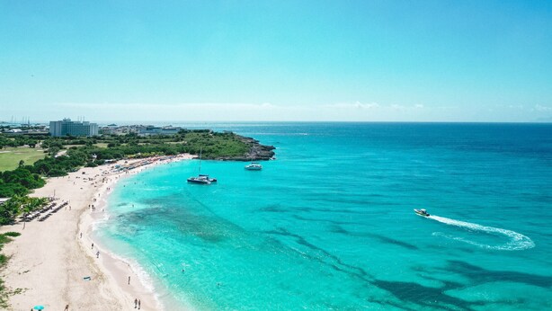 A coastal beach with clear turquoise waters, a sandy shore, and a few boats. - B-1702 Stunning ocean view 2 bedroom (Cupecoy)