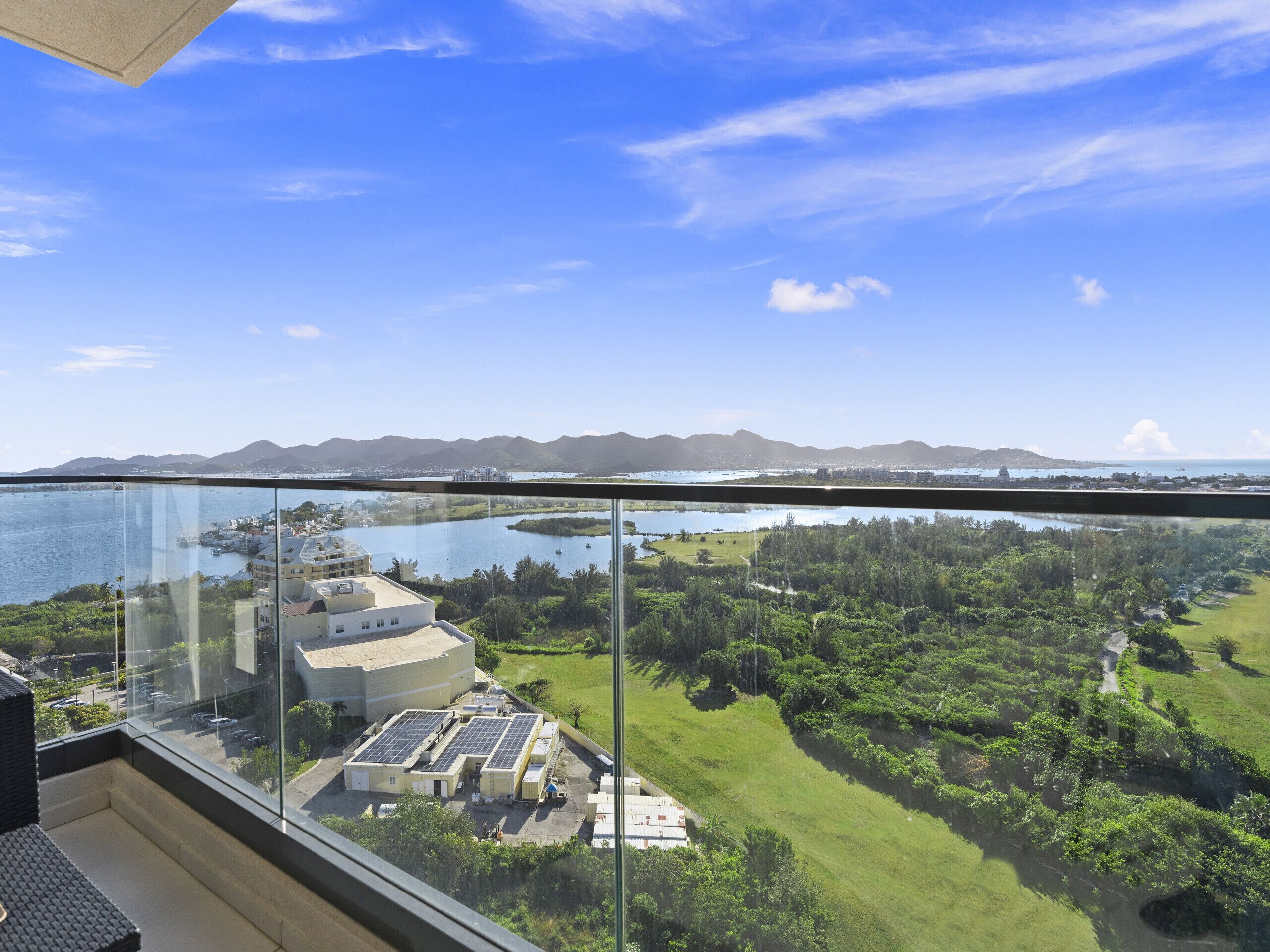 A high-rise building with a view of a body of water, greenery, and distant mountains.