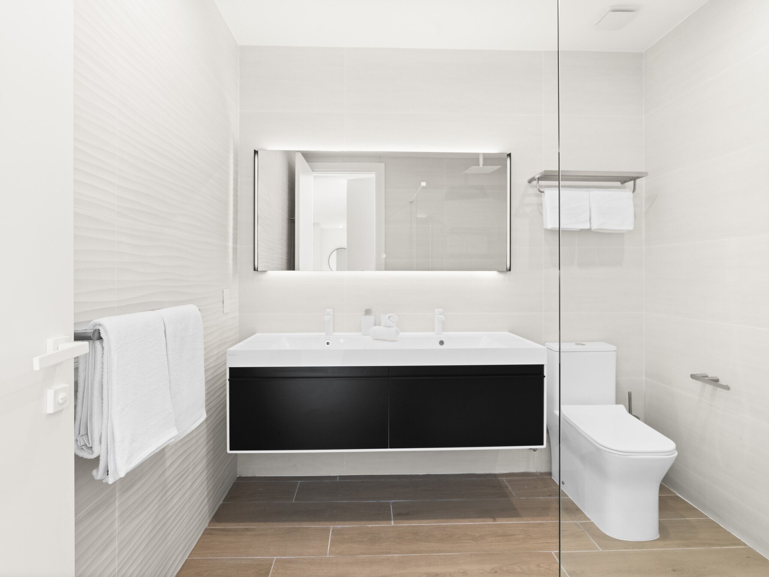 Un bagno moderno con un lavandino bianco capiente, un mobile contenitore nero, un water bianco e un box doccia in vetro.