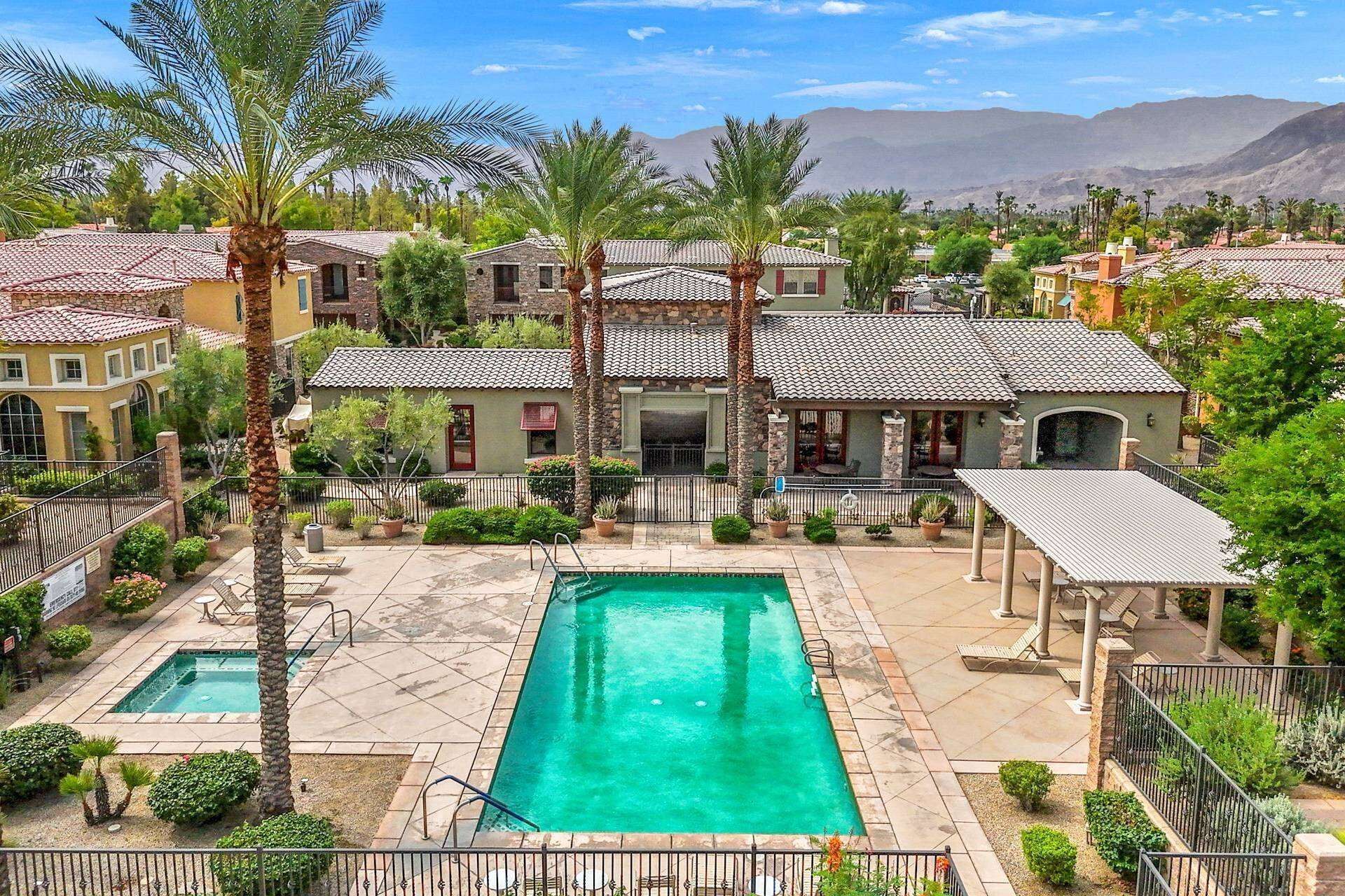 A residential area with a swimming pool, multiple houses with tiled roofs, and palm trees.