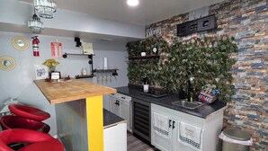 Een kleine keuken met een bar, rode barstoelen, een brandblusser en een decoratieve wand met een 'Welcome Home' bord.