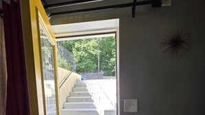 Een open deur die leidt naar een trap, een deurmat, een wandlamp en een gedeeltelijk zicht op een bank.