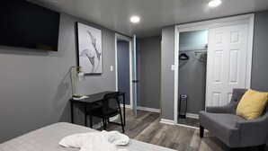 Een moderne slaapkamer met een bed, een bureau, een stoel en een grijze fauteuil.