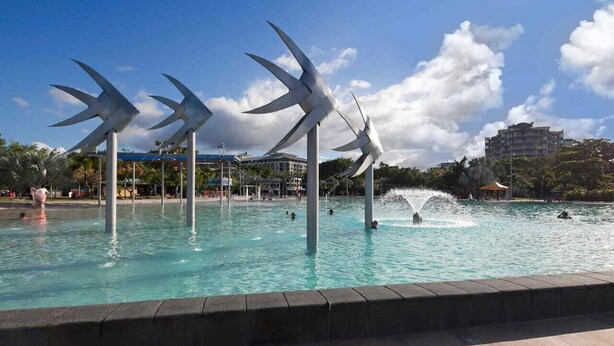 Una piscina con esculturas de molinos, una fuente y un edificio al fondo.