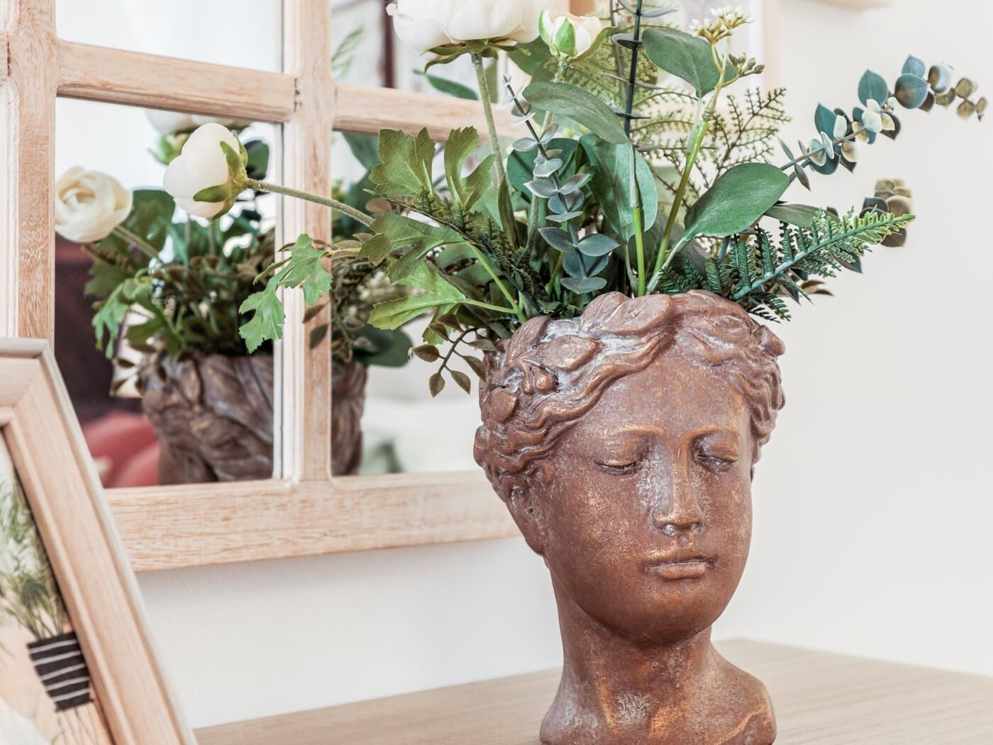 Un vase décoratif orné d’une tête sculptée et surmonté d’un bouquet de fleurs, le tout posé sur une surface en bois.