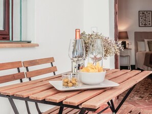 Una mesa de madera con un plato blanco, un cuenco de vidrio con aceitunas y dos copas de vino junto a una botella.